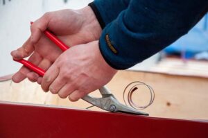 Händer håller i verktyg som bearbetar plåt. Bild av Oskarssons Plåtslageri.